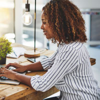 A woman with curly hair smiling as she's using a laptop. 