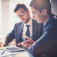 Two businessmen looking over notes on a tablet.