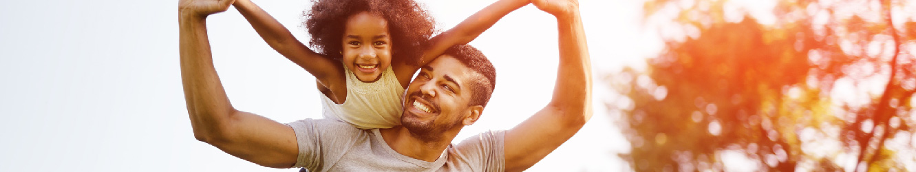 Dad holding his daughter up over his shoulders outside, they are smiling. 