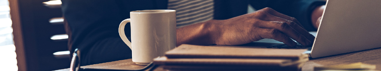 Close up shot of hands typing on a laptop. There's a coffee cup sitting next to it.