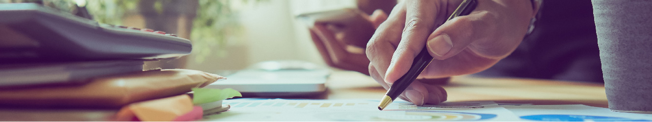 Close up of hands holding a pen pointing at documents on a table.